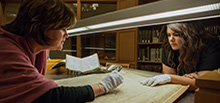 Two female students examining an old book with protective gloves in the library.