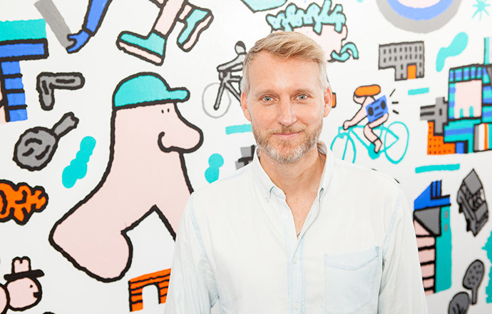 Brooklyn College Assistant Professor of English Matthew Burgess '01 M.F.A. stands in front of the work of artist and collaborator Josh Cochran, a mural that is a part of Burgess' Poetry Urban Mural Project (PUMP). Photo by Craig Stokle.